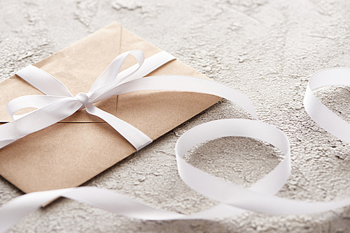 selective focus of beige envelope with white ribbon on grey textured surface