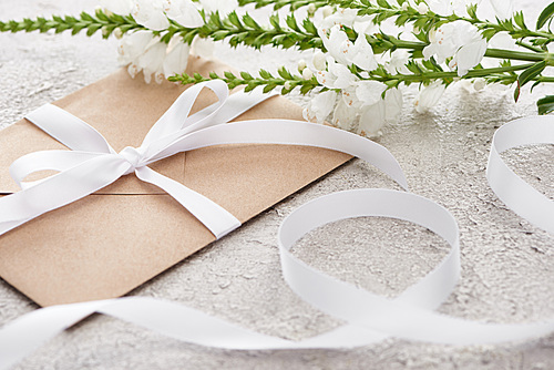 selective focus of beige envelope with ribbon near white flowers on textured surface