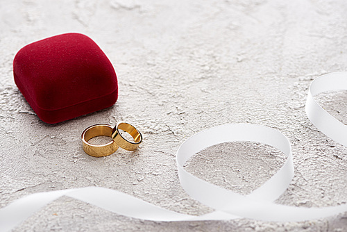 golden rings near red gift box and white ribbon on textured surface