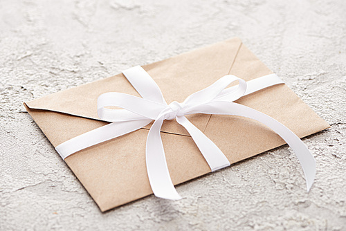 beige envelope with white ribbon on grey textured surface