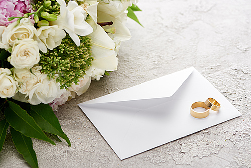 wedding rings on white envelope near bouquet of flowers on textured surface