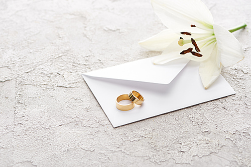 two golden wedding rings on envelope near white lily on textured surface