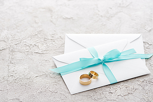 two golden rings on white envelopes with blue ribbon on textured surface