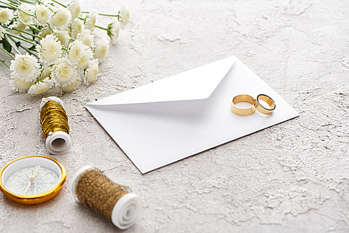 golden rings on white envelope near bobbins, chrysanthemums and golden compass on textured surface