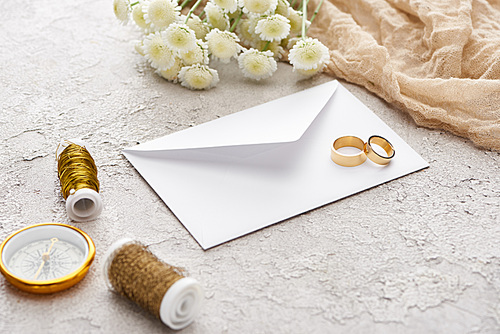 golden rings on white envelope near bobbins, chrysanthemums, beige sackcloth and golden compass on textured surface