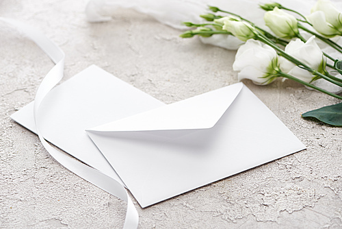 white envelope near eustoma flowers and white ribbon on grey textured surface
