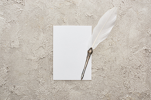 top view of quill pen on white empty card on grey textured surface