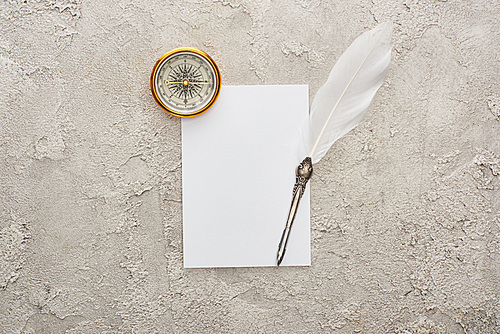 top view of quill pen on white card near golden compass on grey textured surface