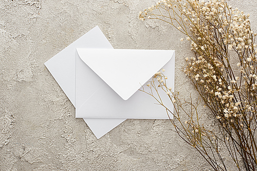 top view of piece of white envelope and card near flowers on textured surface