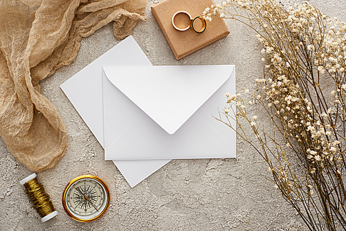 top view of envelope near beige sackcloth, golden compass and wedding rings on textured surface