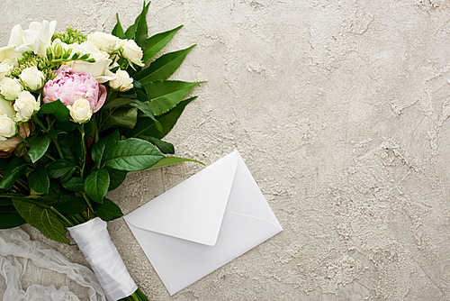 top view of bouquet of flowers near white envelope on textured surface