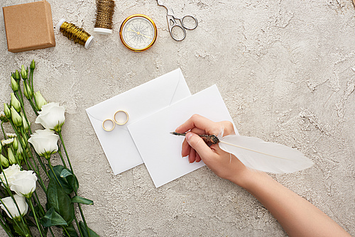 cropped view of woman writing on empty card near wedding rings, compass, scissors, bobbins and eustoma flowers on textured surface