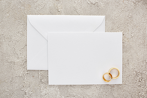 top view of golden wedding rings on blank invitation card on textured surface