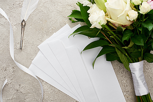 top view of envelopes near bouquet, white ribbon and quill pen on grey textured surface