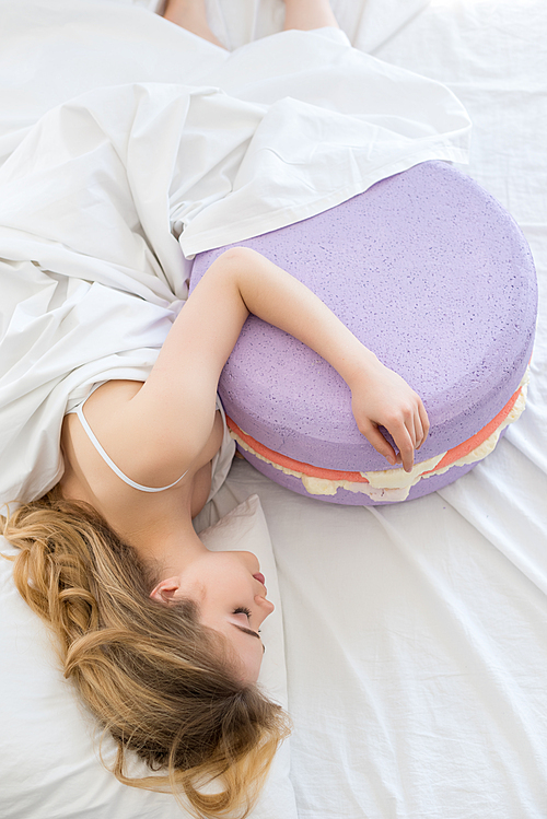top view of beautiful girl sleeping with big purple macaron on bed