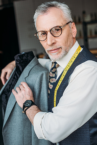 handsome tailor hugging mannequin with jacket at sewing workshop
