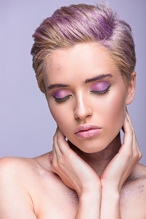 attractive woman with violet glitter on neck and short hair touching neck with closed eyes isolated on violet