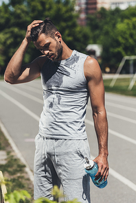 handsome young man in wet shirt with fitness bottle on running track