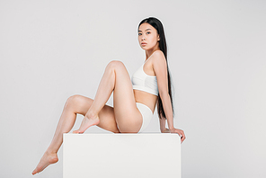 elegant asian girl posing in lingerie on white cube, isolated on grey