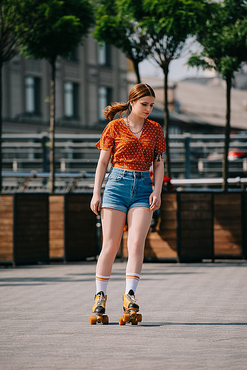 beautiful stylish girl in denim shorts roller skating on street