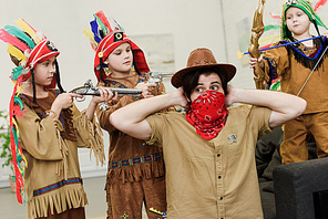 father in hat and bandana and little sons in indigenous costumes with toys playing together at home