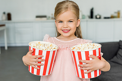 adorable little child holding boxes with popcorn and smiling at camera
