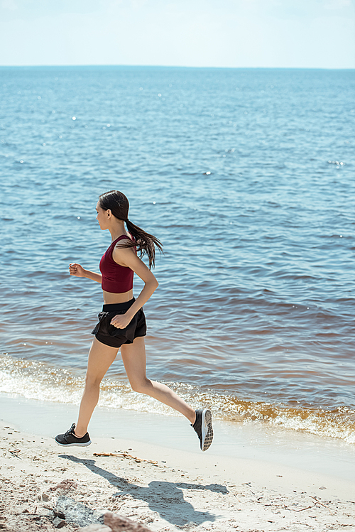 side view of young asian sportswoman running on beach