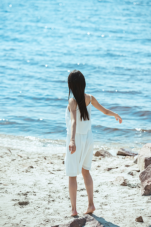 rear view of woman in white dress dancing on beach by sea
