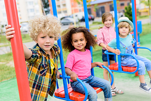 multicultural group of little children riding on swings at playground