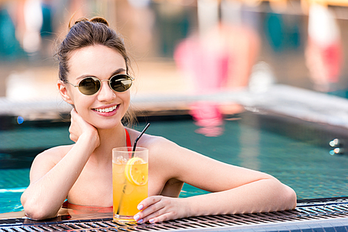 attractive young woman with delicious orange cocktail relaxing at poolside