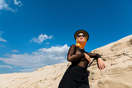 bottom view of elegant woman posing near sand dune with blue sky on background