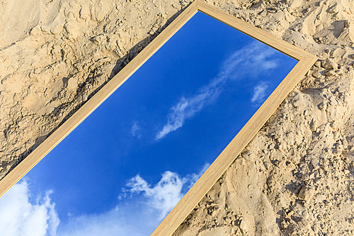 mirror with reflection of blue cloudy sky lying on sand