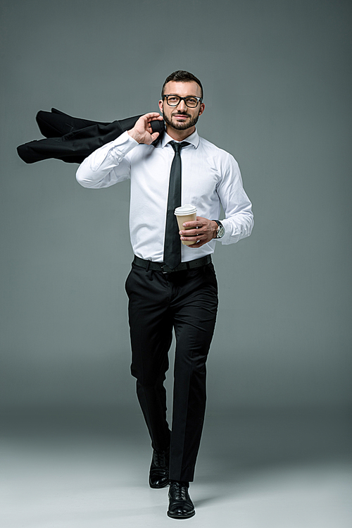 handsome businessman walking with disposable coffee cup on grey