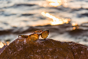 close-up view of sunglasses in stone on sea coast at sunset