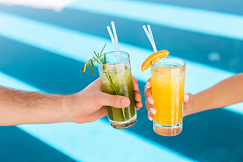 cropped view of couple holding glasses with fresh lemonades at swimming pool