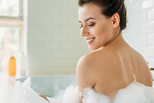 beautiful smiling naked girl sitting in bathtub with foam