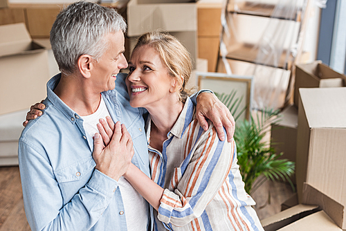 high angle view of happy senior couple embracing, holding hands and smiling each other in new home
