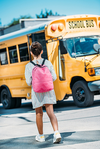 rear view of schoolgirl with backpack standing in front of school bus