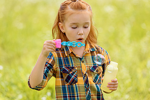 portrait of kid blowing soap bubbles in meadow