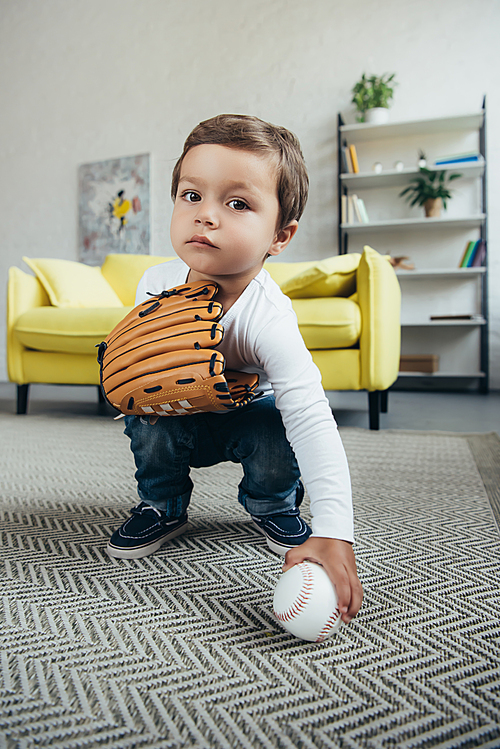 adorable kid playing with baseball glove and ball at home