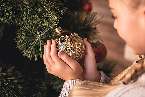 cropped image of adorable preteen kid holding golden bauble in hands at home