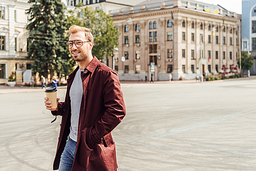 handsome man in autumn outfit walking with disposable coffee cup in city