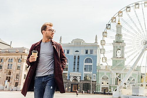 handsome man in autumn outfit walking with disposable coffee cup near observation wheel