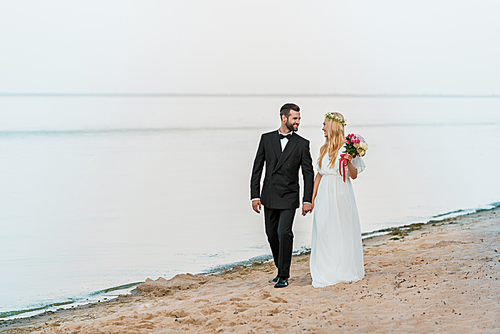 wedding couple holding hands, walking and looking at each other on beach