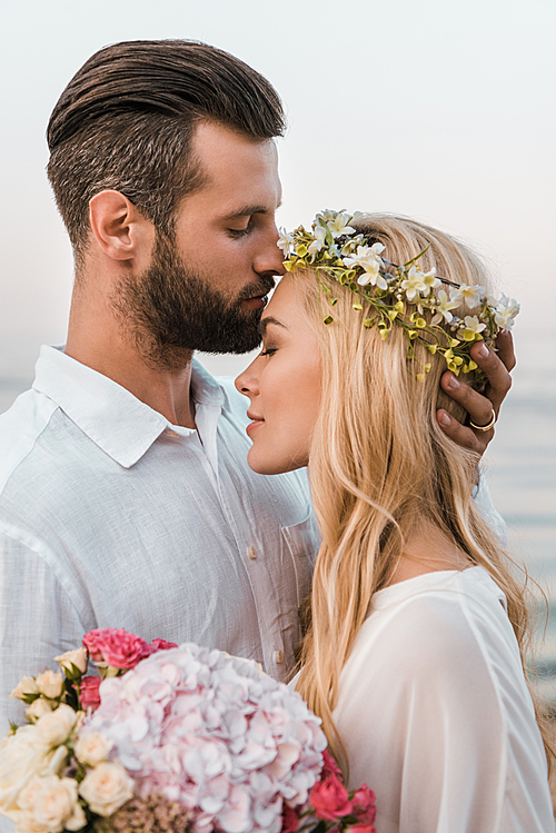 portrait of handsome groom kissing beautiful bride forehead on beach
