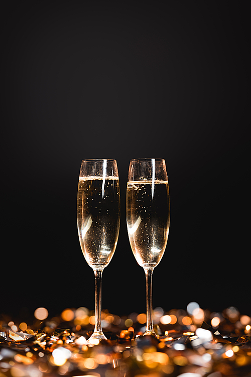 new year celebration with champagne glasses on golden confetti on black