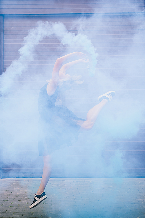 young female contemporary dancer dancing in blue smoke on street