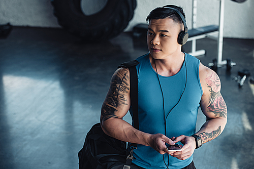 young asian sportsman using smartphone and listening to music in gym
