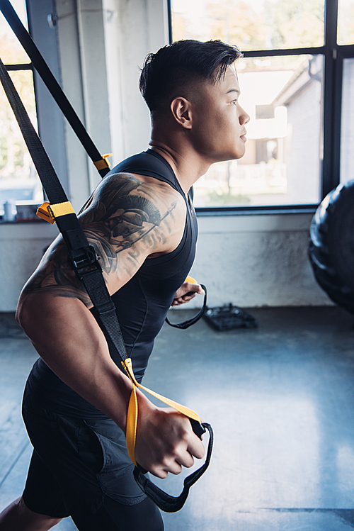 side view of young muscular sportsman training with resistance bands in gym