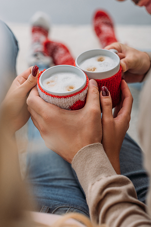 cropped image of couple holding cups of cappuccino at home, christmas concept